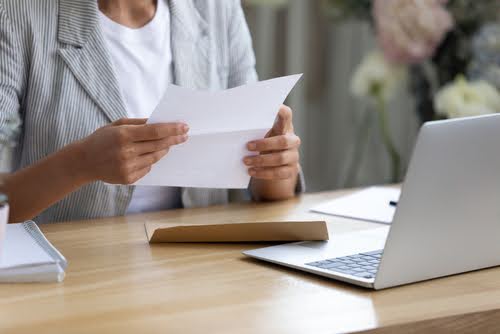 Person holding letter in front of computer at desk.